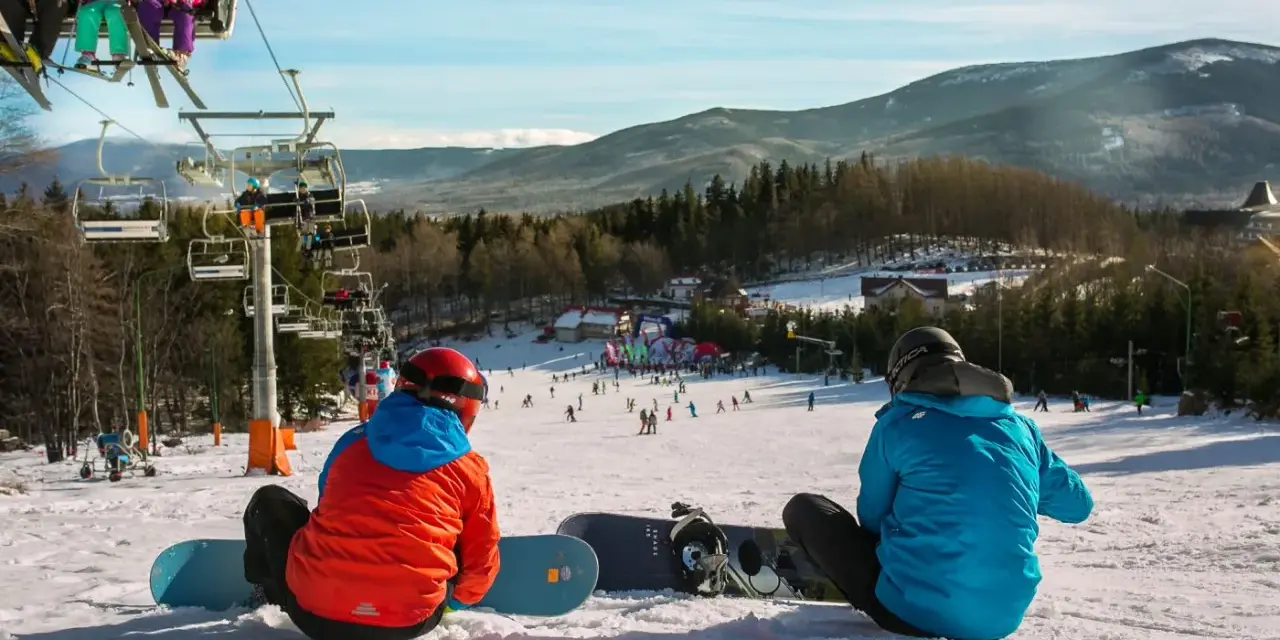 Dwaj snowboardziści odpoczywają na stoku, w tle widać wyciąg narciarski Karpacz i góry.