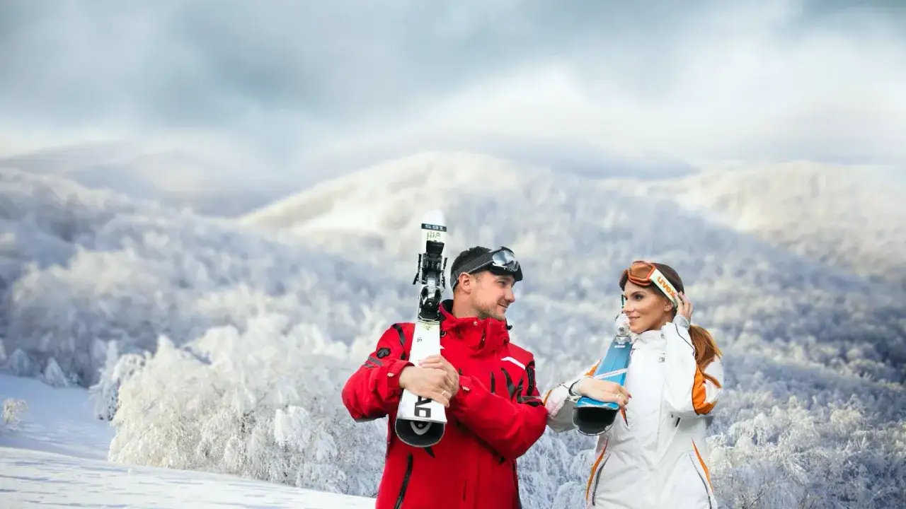 Para, gotowi na jazdę, od kiedy otwarte stoki narciarskie. W tle zimowy krajobraz.